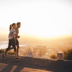 Shot van een jong stel dat loopt op een heuvel weg buiten de stad. Jonge man en vrouw joggen in de ochtend met fel zonlicht. door Jacob Lund (bron: Shutterstock)