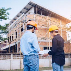 Two engineering man with helmet and paper work are discussing about the project over construction site background. door Freedom Studio (Shutterstock)