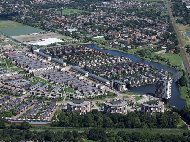 Aerial view of a new district in Alkmaar, Netherlands with a lot of colorful houses. The district is called VROONERMEER and a lot of buildings have solar panels. In the back it's Sint Pancras. door Aerovista Luchtfotografie (bron: shutterstock)