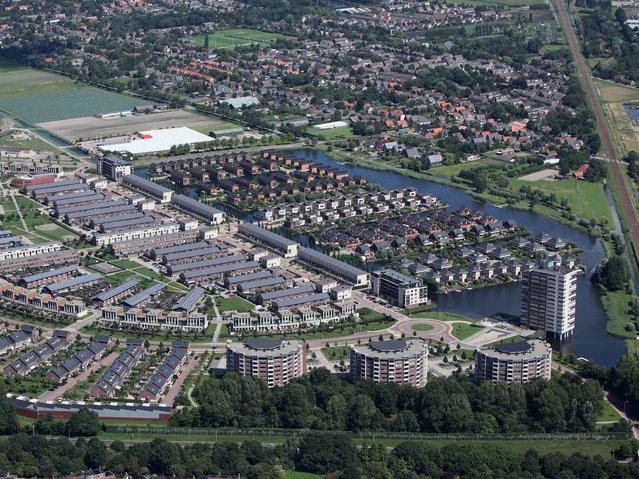 Aerial view of a new district in Alkmaar, Netherlands with a lot of colorful houses. The district is called VROONERMEER and a lot of buildings have solar panels. In the back it's Sint Pancras. door Aerovista Luchtfotografie (bron: shutterstock)
