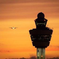 Airport control tower with a airplane landing in the background during sunset. door VanderWolf Images (shutterstock)
