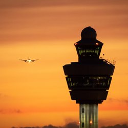 Airport control tower with a airplane landing in the background during sunset. door VanderWolf Images (bron: shutterstock)