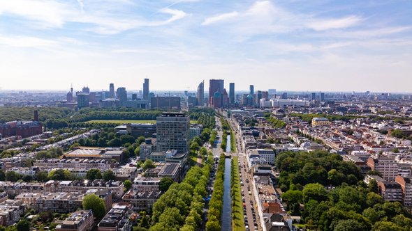 Hoog zicht op de Haagse stad met moderne gebouwen, groene ruimtes, een gracht en geparkeerde auto’s op een zonnige zomerdag in Nederland door 21 Aerials (bron: shutterstock)