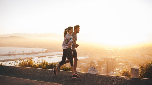 Shot van een jong stel dat loopt op een heuvel weg buiten de stad. Jonge man en vrouw joggen in de ochtend met fel zonlicht. door Jacob Lund (bron: Shutterstock)