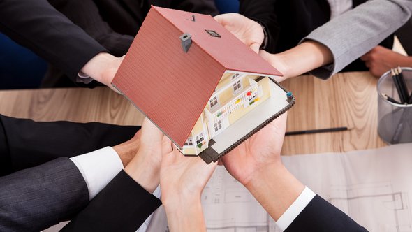 Multiple hands of diverse business people supporting a model house conceptual of partnership and teamwork door Andrey_Popov (bron: Shutterstock)