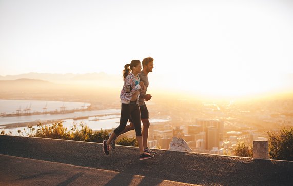 Shot van een jong stel dat loopt op een heuvel weg buiten de stad. Jonge man en vrouw joggen in de ochtend met fel zonlicht. door Jacob Lund (bron: Shutterstock)