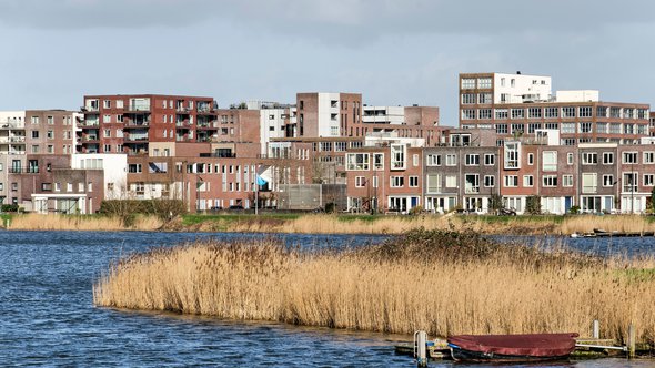 Amsterdam, The Netherlands, February 11, 2022: view across a lake with reeds-lined banks towards a modern neighbourhood with mailnly brick housing in IJburg district door Frans Blok (bron: shutterstock)