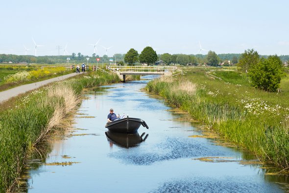 A small boat on the water and cyclists along the water in the nature reserve at Nijkerk. door Jan van der Wolf (bron: Shutterstock)