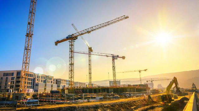 Grote bouwplaats met meerdere kranen die werken aan een bouwcomplex, met helderblauwe lucht en de zon door Smileus (bron: Shutterstock)