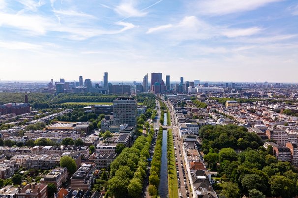 Hoog zicht op de Haagse stad met moderne gebouwen, groene ruimtes, een gracht en geparkeerde auto’s op een zonnige zomerdag in Nederland door 21 Aerials (bron: shutterstock)