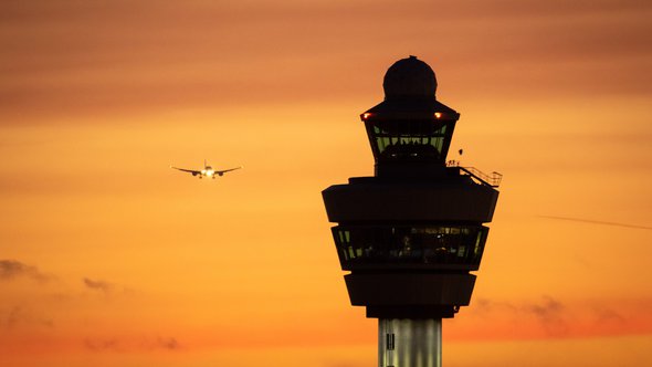 Airport control tower with a airplane landing in the background during sunset. door VanderWolf Images (bron: shutterstock)